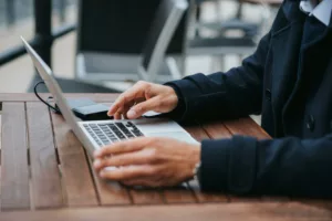 Une personne tapant sur un ordinateur portable posé sur une table en bois à l'extérieur.