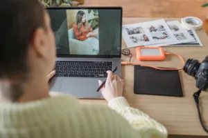 Photographe retouchant une photo sur ordinateur portable avec tablette graphique et appareil photo numérique posé sur le bureau.