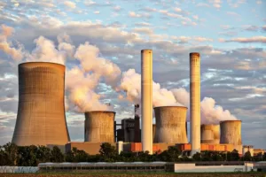 Vue d’une centrale nucléaire avec tours de refroidissement et panaches de vapeur au coucher du soleil.