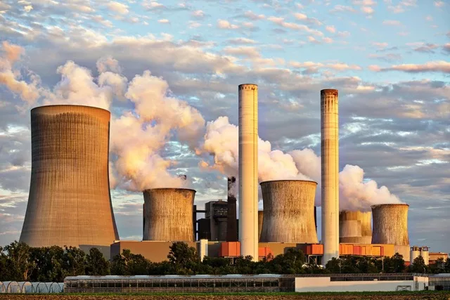 Vue d’une centrale nucléaire avec tours de refroidissement et panaches de vapeur au coucher du soleil.